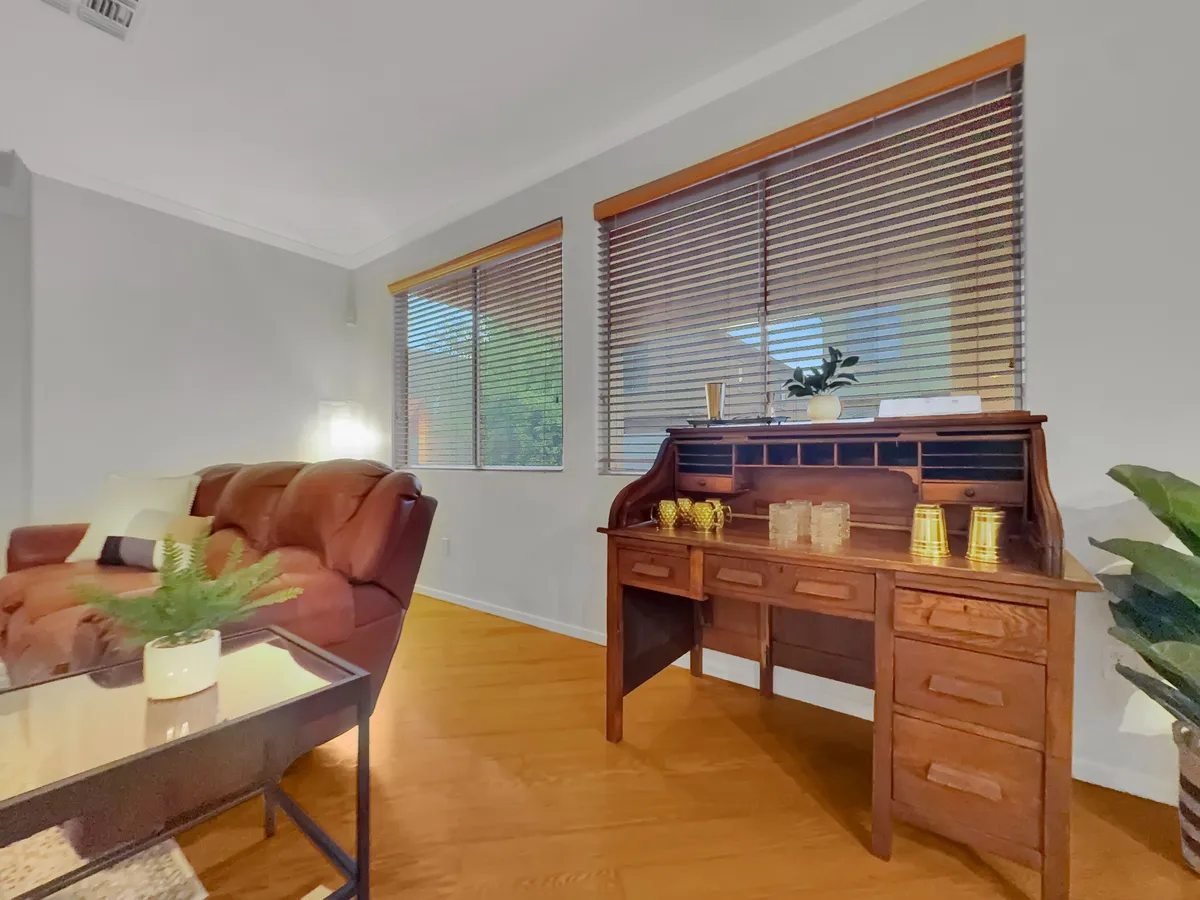 A bright spot featuring a comfortable brown leather sofa beside a wooden desk, with sunlight streaming in through the windows—ideal for daytime reading, working remotely, or unwinding in peace.
