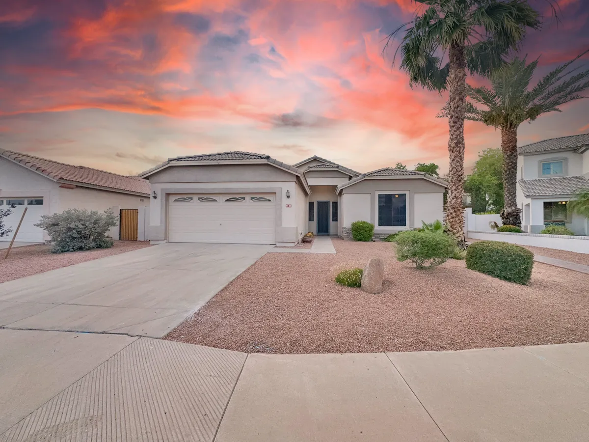 The front facade of the home is framed by palm trees and a landscaped garden, set against a dramatic sunset sky. The spacious front yard and porch offer space for gatherings and a welcoming entry to the neighborhood.