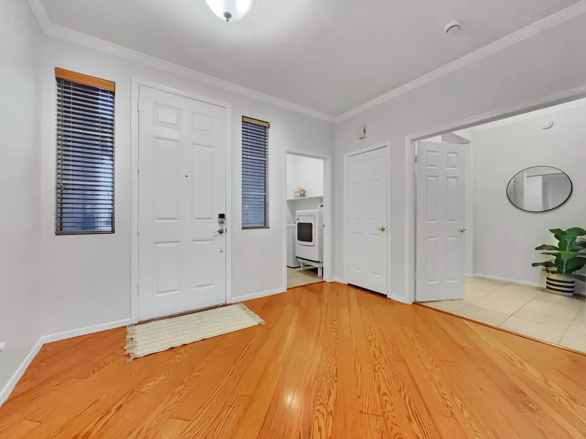 An inviting entryway with a front door, wooden floor, windows, a mirror, and a plant. The scene evokes a warm welcome for guests entering the home, setting the tone for a memorable stay.