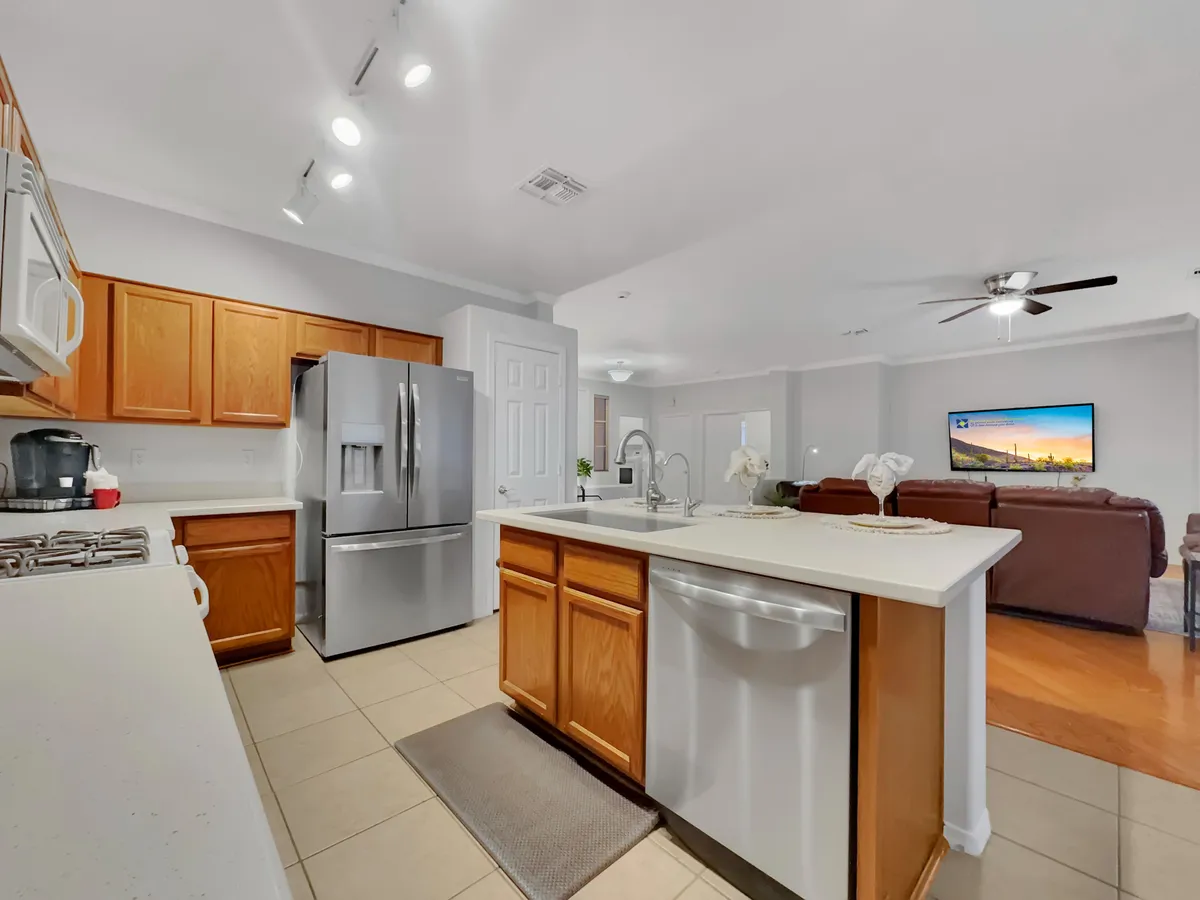This image centers on a kitchen island, surrounded by stainless steel appliances and an open living area. Decorative plants bring warmth to the modern space, and the kitchen is visibly clean and well-organized, perfect for preparing meals or entertaining guests.