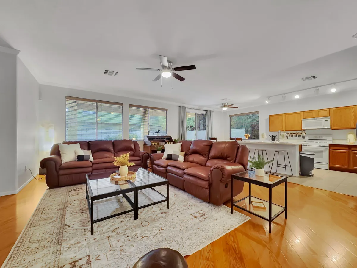 A spacious living area featuring brown leather sofas arranged around a glass coffee table and area rug, with a kitchen island visible in the background. The room is warmly lit and designed for gatherings or relaxing after a day of adventure.