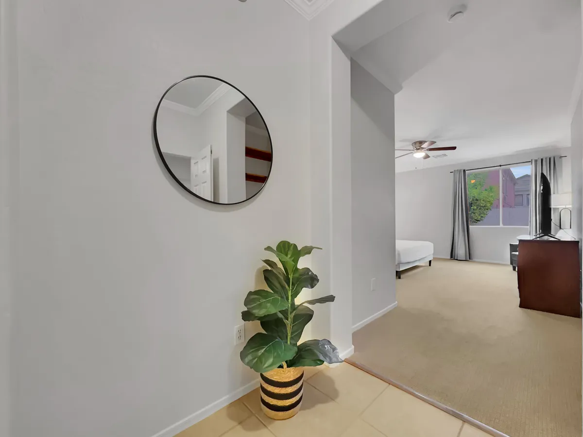 A vignette of a round mirror, potted plant, and a window with curtains fills this bright, inviting corner. The scene radiates warmth and the gentle transition between indoor and outdoor environments.