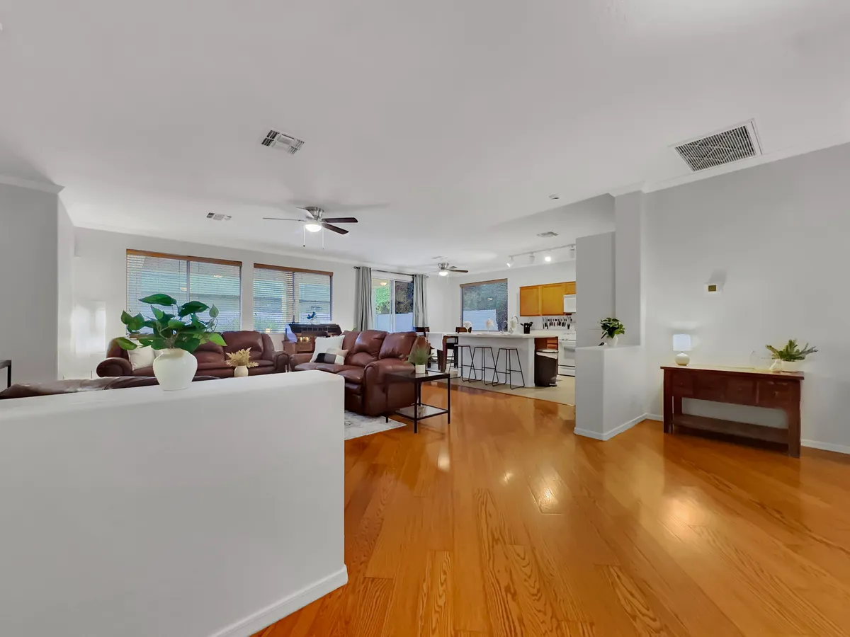 This image highlights a welcoming space with brown leather sofas, a kitchen island, wooden floors, and green plants. The open space is ideal for family meals, relaxation, and social gatherings, blending the kitchen and living spaces with a modern touch.