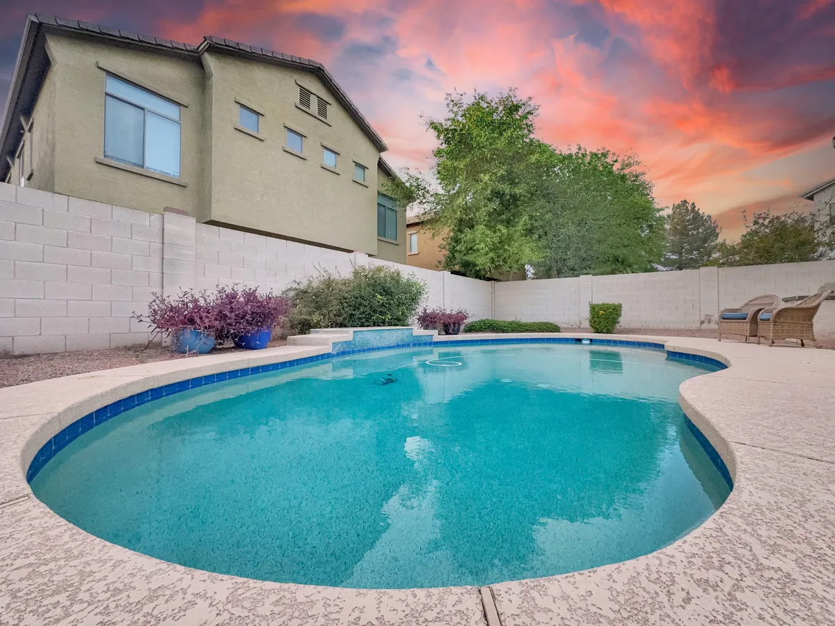 A sparkling swimming pool is surrounded by lush landscaping and colorful plants, set beneath a clear blue sky. The inviting pool area is complemented by greenery and comfortable spaces for lounging, creating a vibrant and family-friendly backyard retreat.