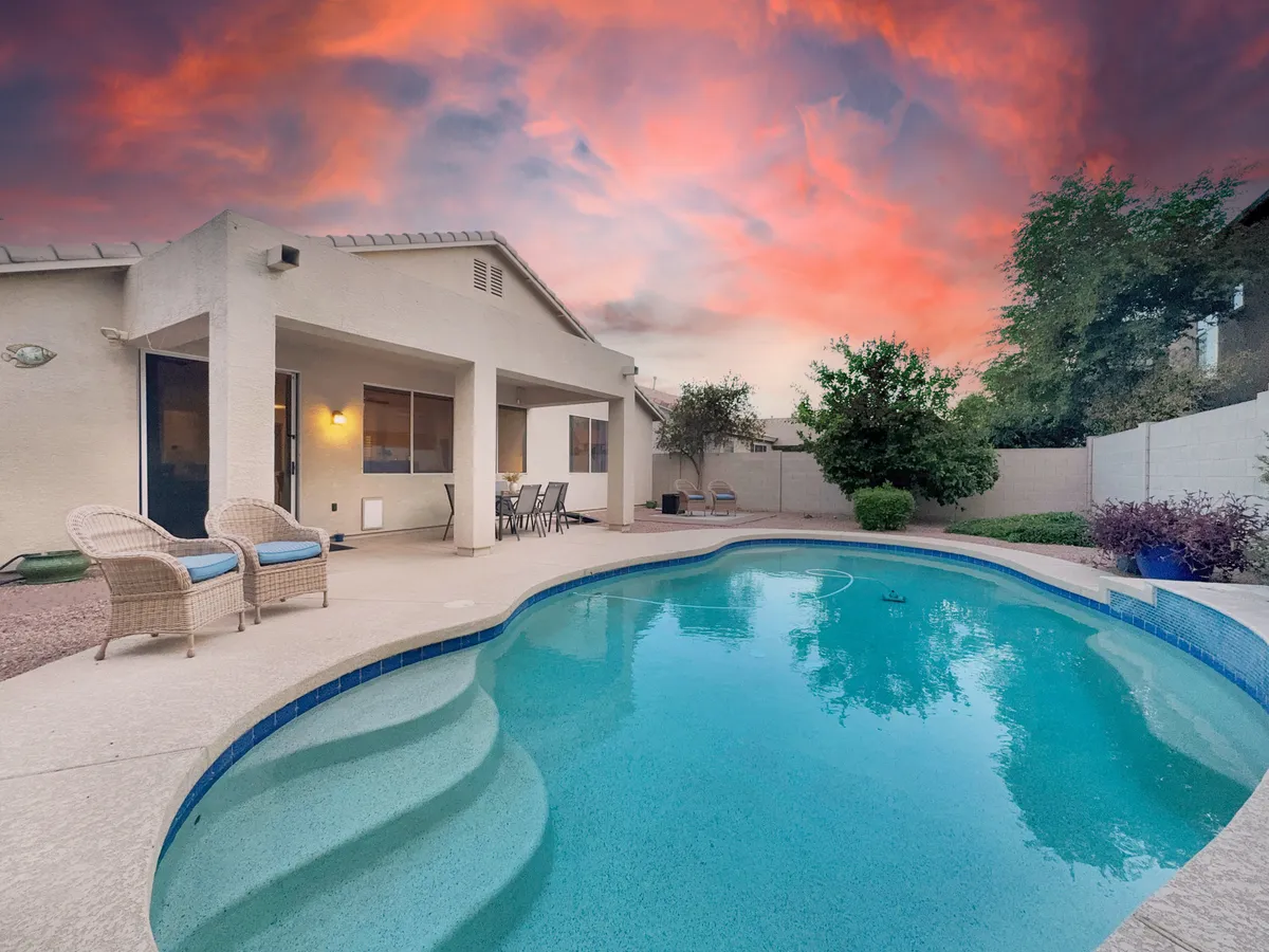 A cheerful backyard patio with a shimmering swimming pool, inviting outdoor seating, and a spacious area ideal for relaxation or casual gatherings. The patio is designed for both sun-soaked leisure and lively social events.