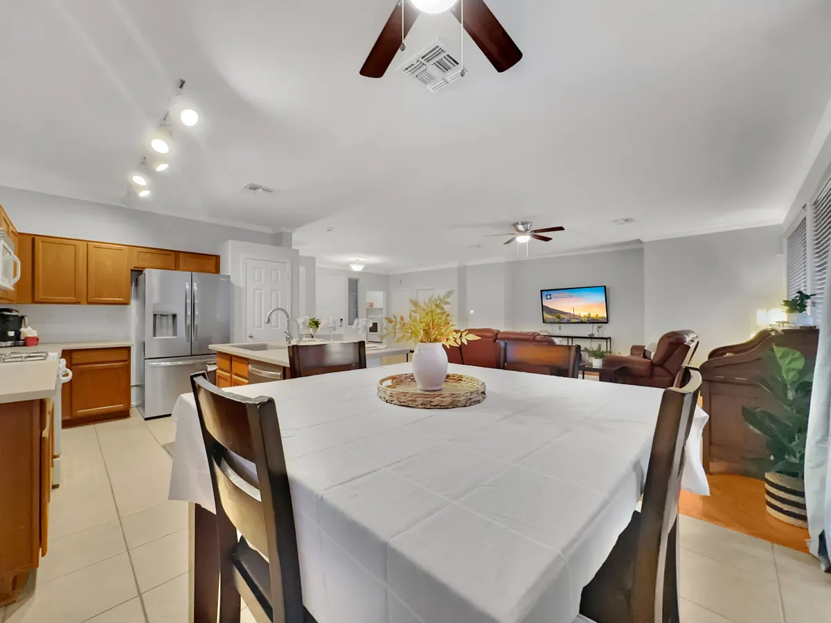 This image features a spacious open-concept area that combines the dining table, kitchen appliances, living area seating, and a television. The layout highlights how the different gathering spaces flow seamlessly together, inviting family meals, social gatherings, and relaxation. Natural light fills the area, enhancing the sense of modernity and comfort.