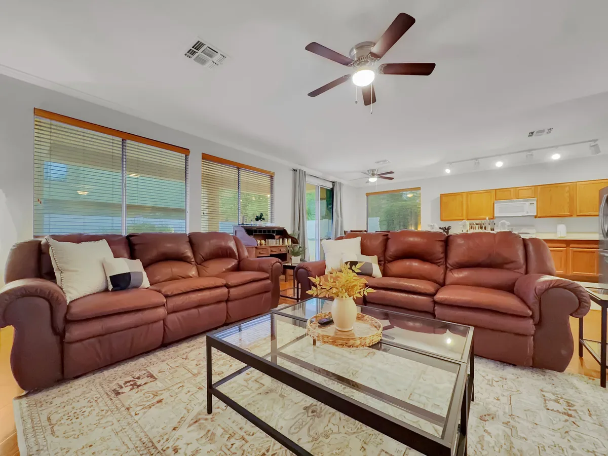 A cozy living area with brown leather sofas and a glass coffee table, with the kitchen area visible in the background. The connection between the seating and cooking spaces highlights an open-plan design ideal for entertaining and socializing.