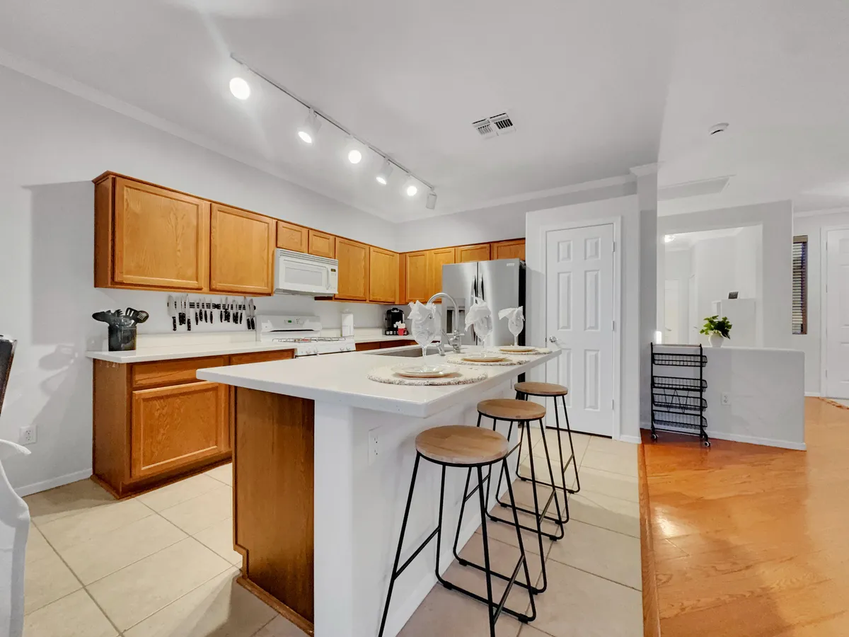 A welcoming kitchen scene featuring a spacious island with stools, well-organized cabinets, and visible appliances. The layout invites social cooking and casual dining experiences, highlighting a functional and attractive culinary space.